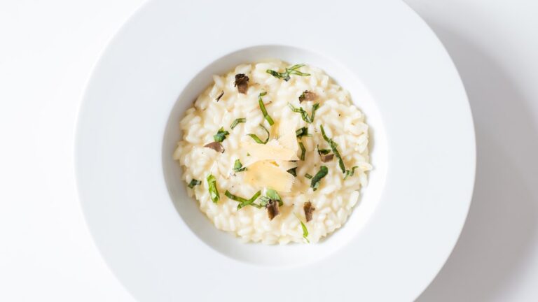 A wide bowl of vegan kent pumpkin risotto topped with crispy fried sage leaves and toasted pine nuts