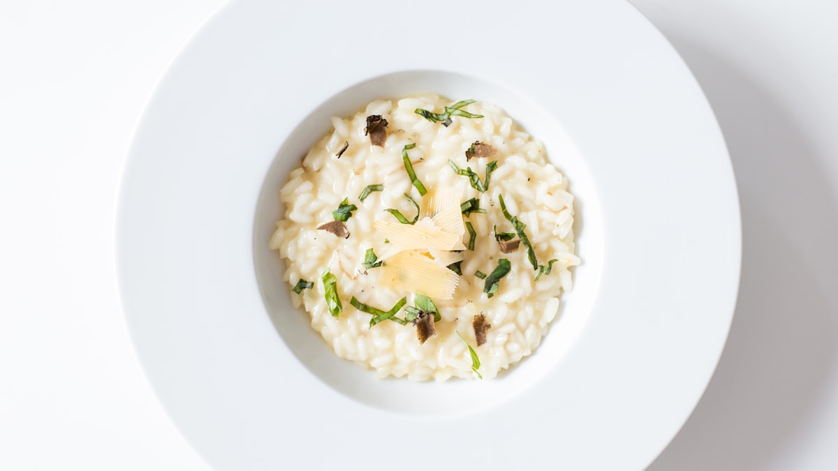 A wide bowl of vegan kent pumpkin risotto topped with crispy fried sage leaves and toasted pine nuts